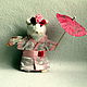 Lia is a white stuffed mouse. She is a Japanese woman, wearing a pink kimono, held in place by a wide belt of polka-dot ribbon adorned with a rose. On his head his hairstyle is made with three roses.